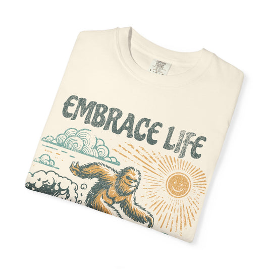 Ivory colored short sleeve t-shirt with embrace lice written on top and a yetti surfing graphic on the front