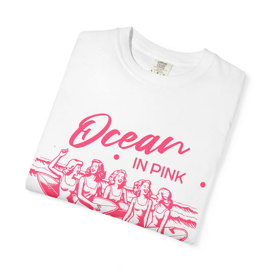 White cotton t-shirt with ocean in pink written on the front with five smiling women holding surf board also in pink