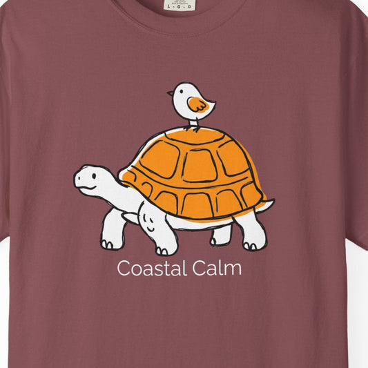Maroon t-shirt with a turtle and bird graphic and 'Coastal Calm' text on a white background