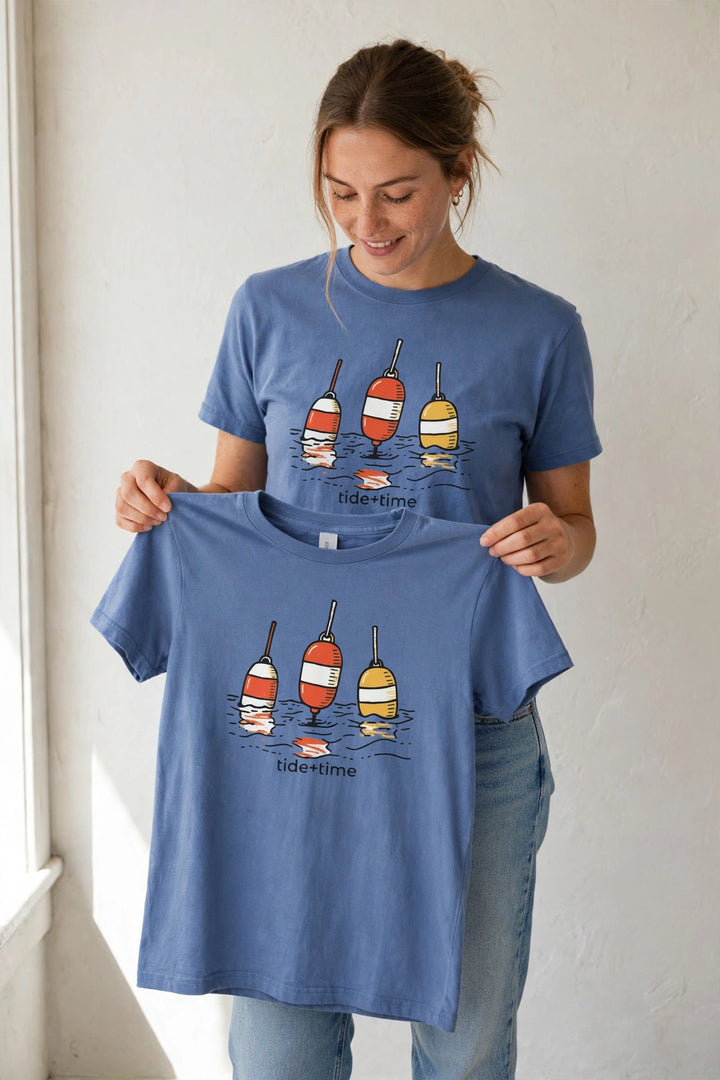 Woman wearing the Beach Buoy Graphic Tee in Mystic Blue, holding up the front print.