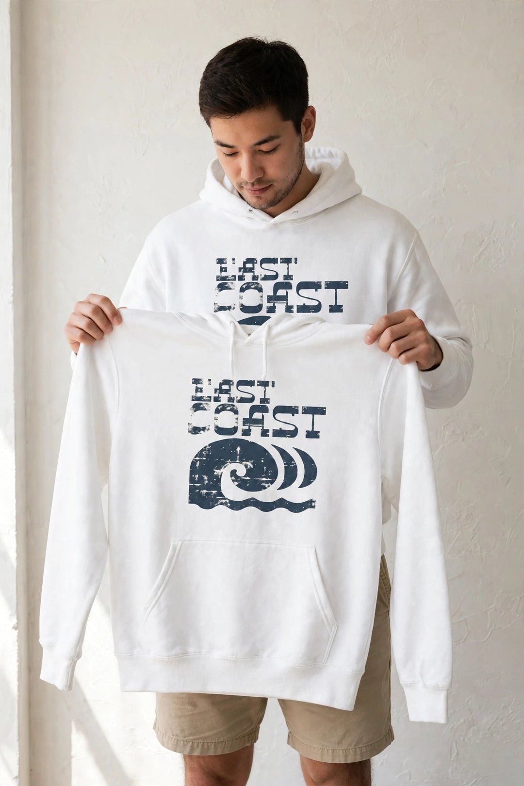 Man wearing the East Coast Waves Hoodie in White, holding up the front print.