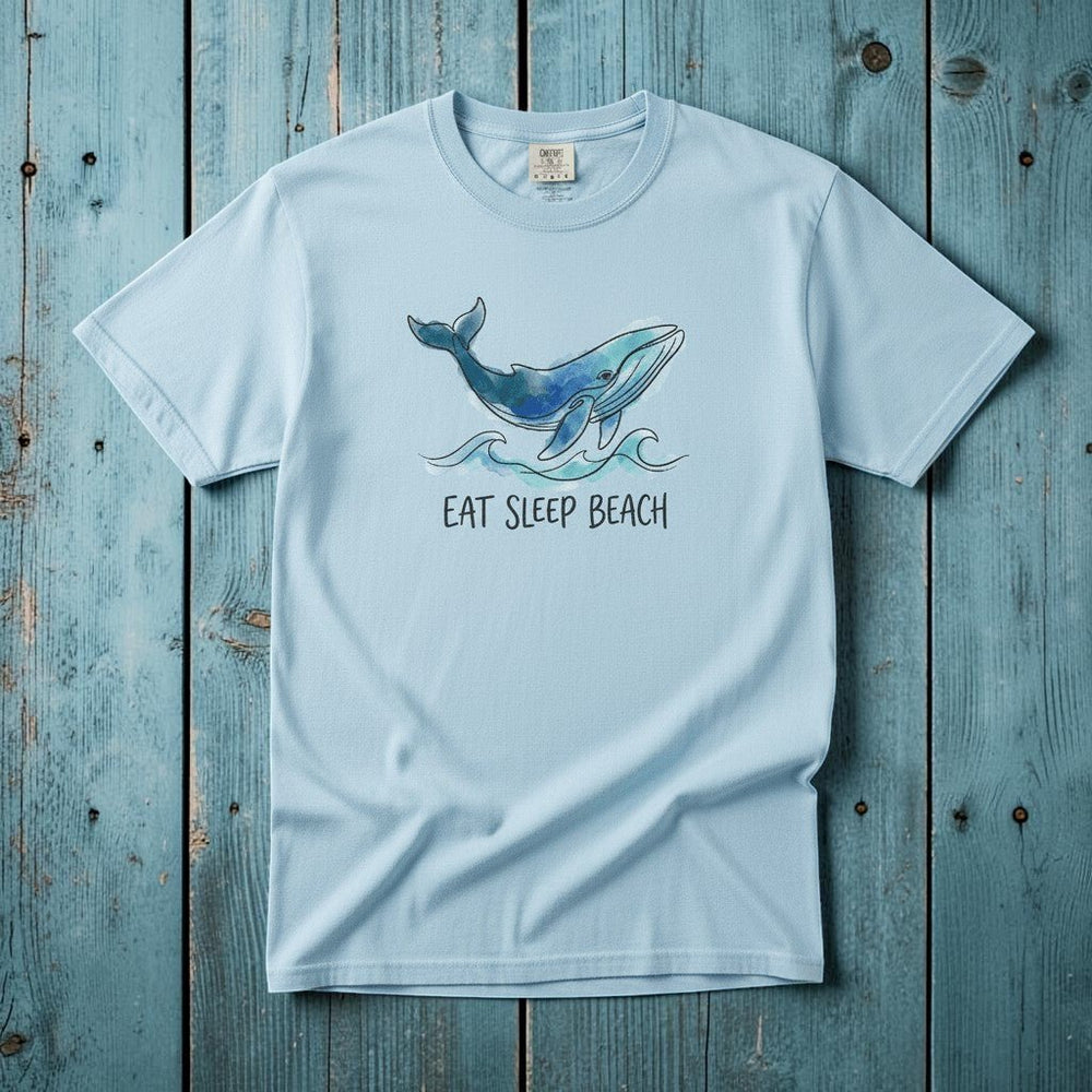 Flat lay - baby blue Eat Sleep Beach tee with Comfort Colors label on weathered driftwood planks