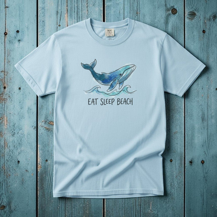 Flat lay - baby blue Eat Sleep Beach tee with Comfort Colors label on weathered driftwood planks