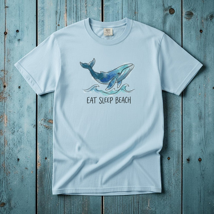Flat lay - baby blue Eat Sleep Beach tee with Comfort Colors label on weathered driftwood planks