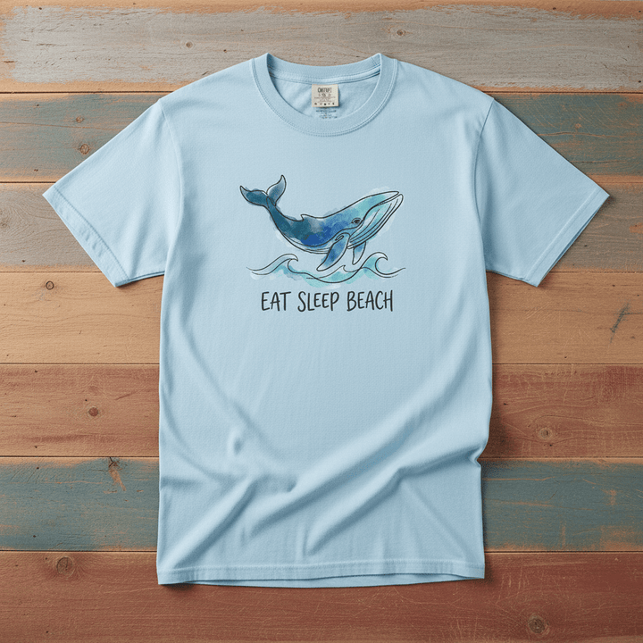 Flat lay - baby blue Eat Sleep Beach tee with Comfort Colors label on weathered driftwood planks