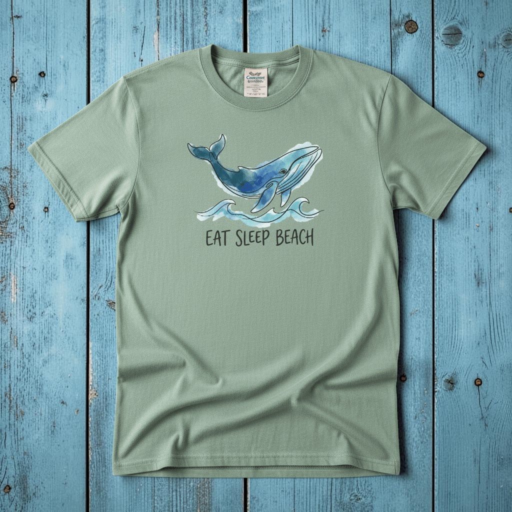 Flat lay - sage green Eat Sleep Beach tee with Comfort Colors label on weathered driftwood planks