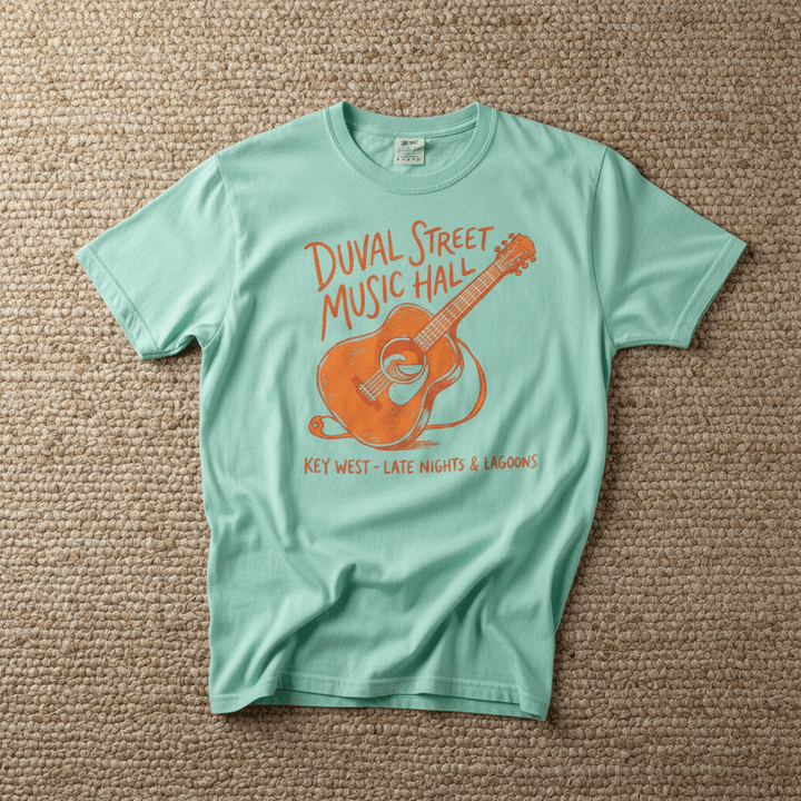 Duval Street Music Hall guitar graphic t-shirt in Island Reef seafoam casually tossed on a light sand-colored woven rug, Key West lifestyle product photo