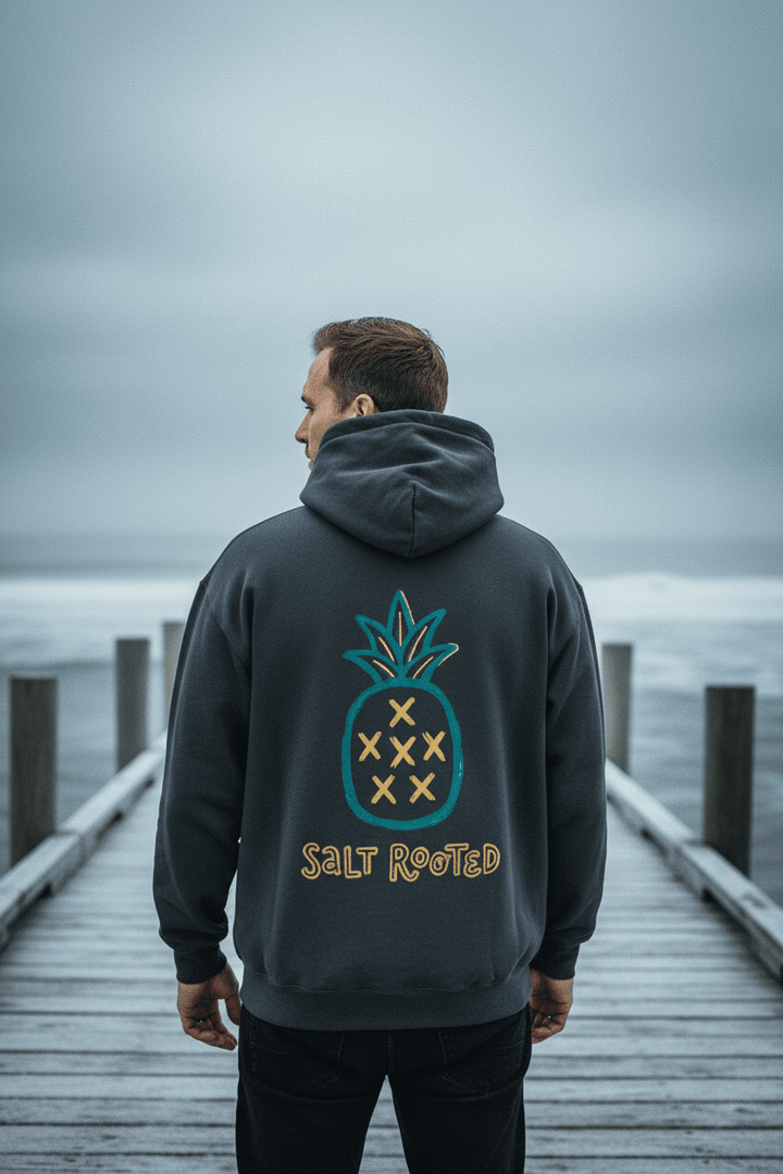 Male model showing back of graphite Salt Rooted pineapple hoodie on frost-dusted bleached wood boat dock