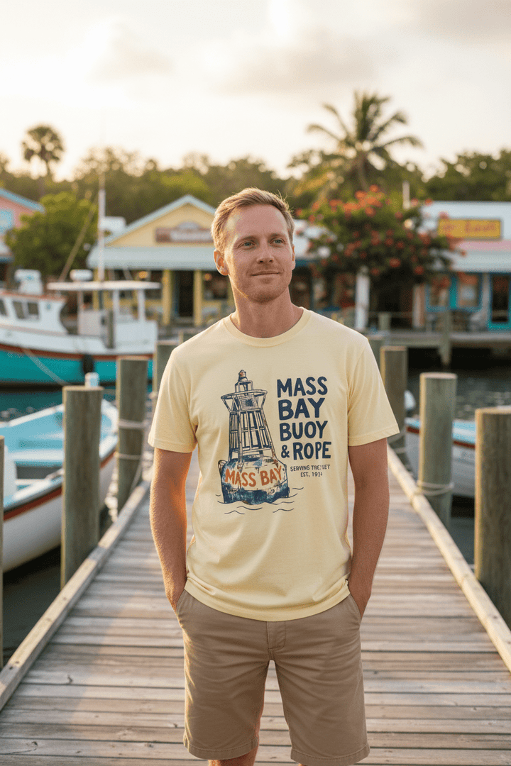 Male model wearing banana cream Mass Bay Buoy &amp; Rope t-shirt on tropical island beach town boat dock