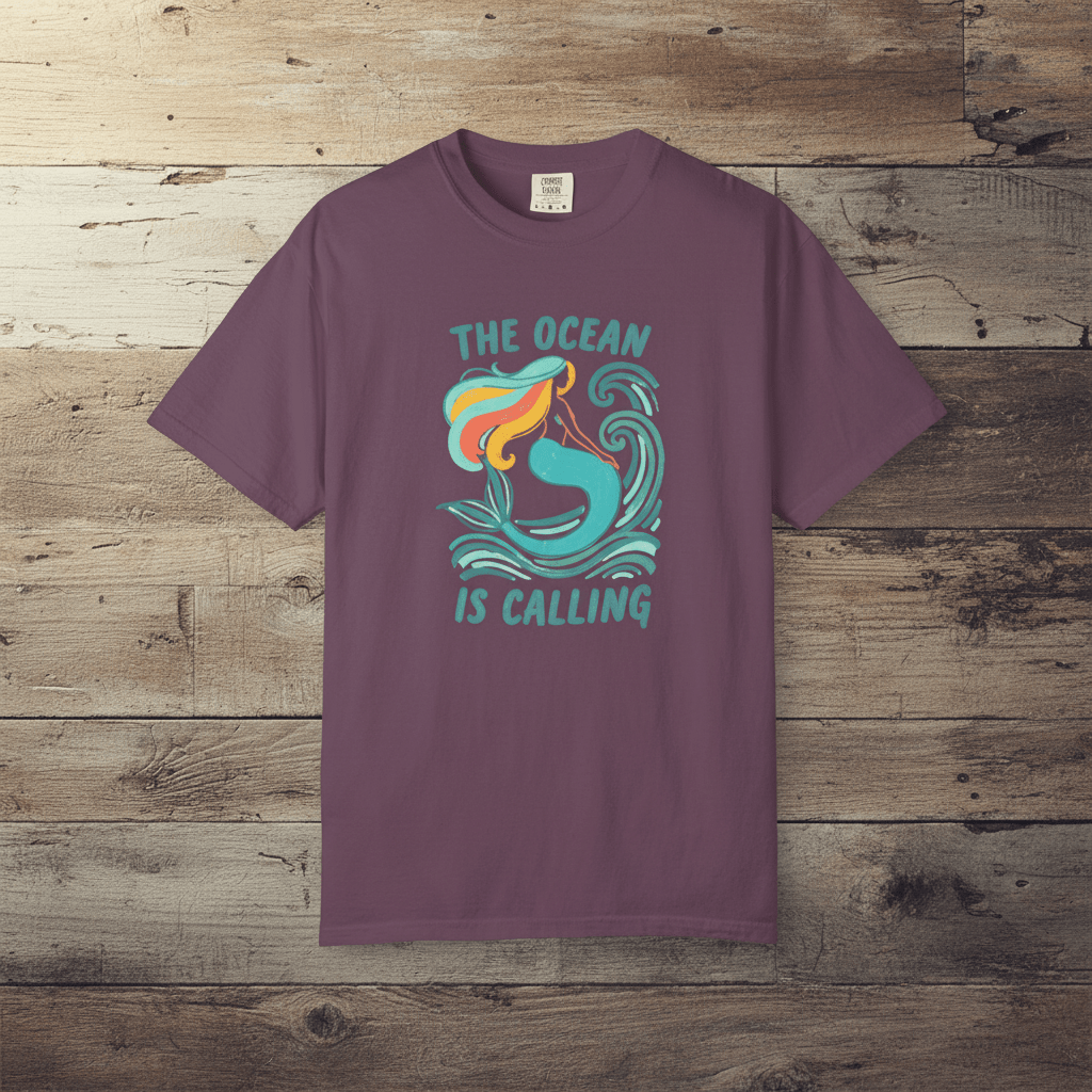 The Ocean Is Calling berry garment-dyed mermaid wave tee laid flat on rustic reclaimed wood