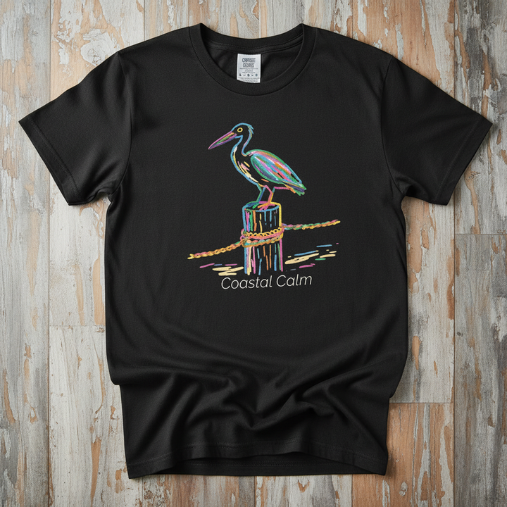 Pelican Pier Coastal Calm black garment-dyed tee on faded driftwood planks