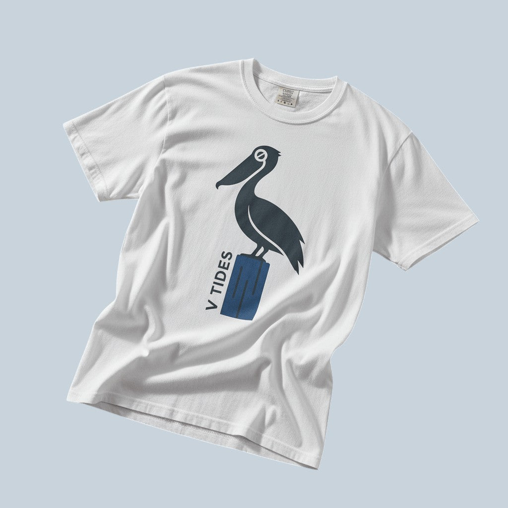 Pelican Dock V Tides coastal graphic t-shirt in White casually tossed on a light sand-colored woven rug, coastal lifestyle product photo