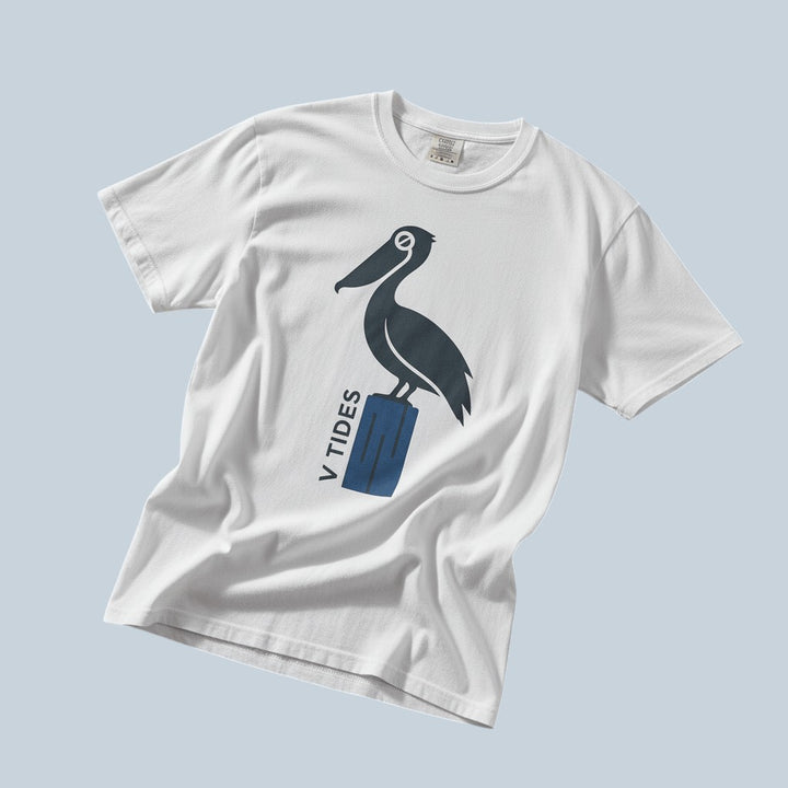 Pelican Dock V Tides coastal graphic t-shirt in White casually tossed on a light sand-colored woven rug, coastal lifestyle product photo