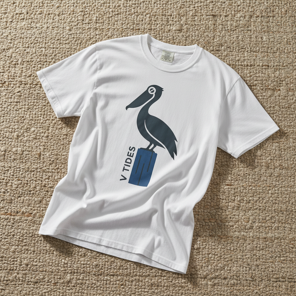 Pelican Dock V Tides coastal graphic t-shirt in White casually tossed on a light sand-colored woven rug, coastal lifestyle product photo