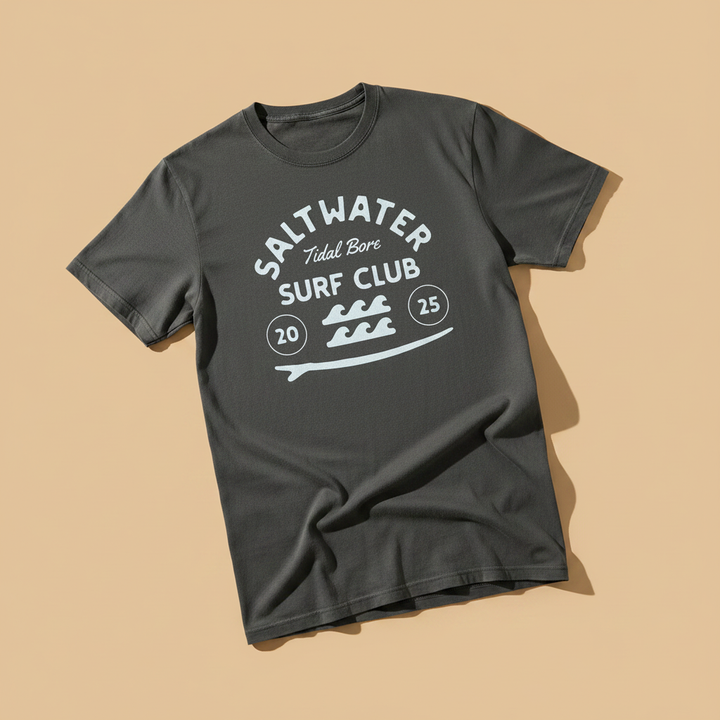 Saltwater Surf Club Tee in Pepper/Charcoal — front graphic, warm sand studio background