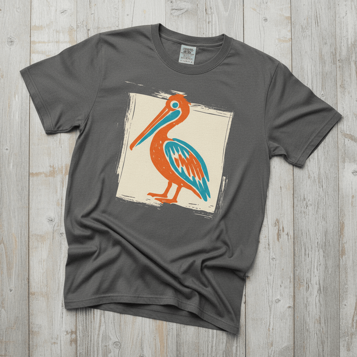 Colorful Beach Pelican pepper garment-dyed tee on faded driftwood planks