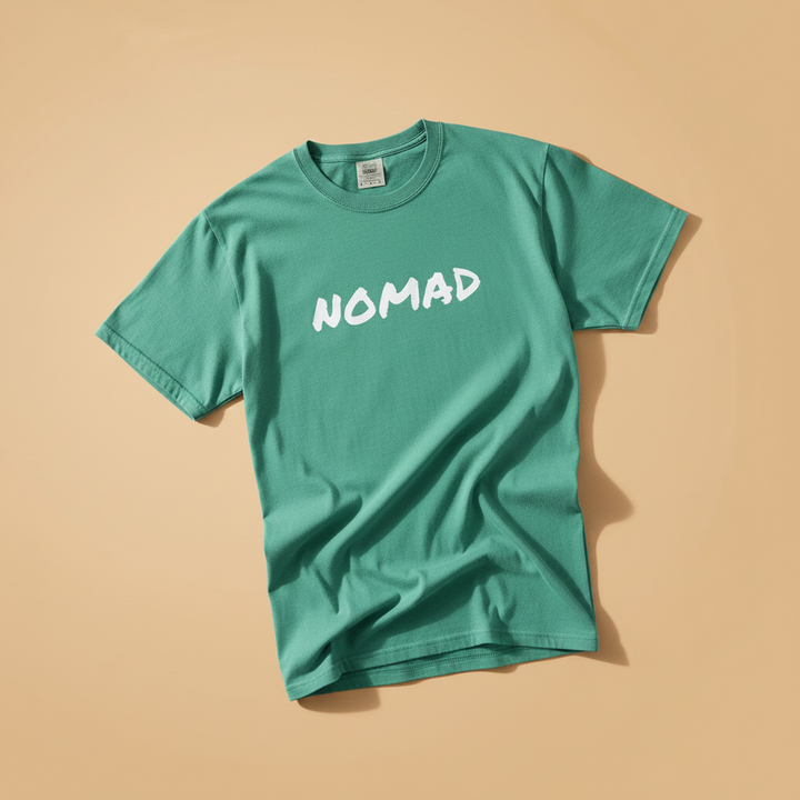 NOMAD Tee in Island Green — front graphic, warm sand studio background