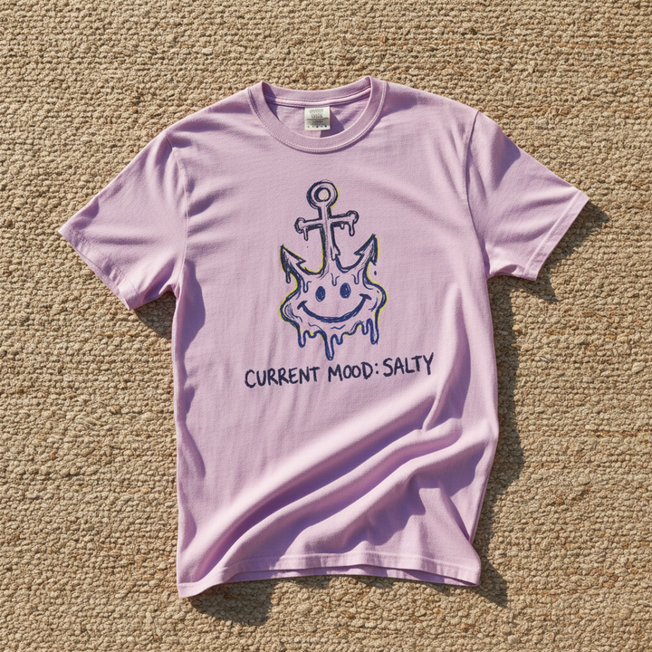 Salty Anchor Current Mood Salty graphic t-shirt in Orchid lavender casually tossed on a light sand-colored woven rug, coastal lifestyle product photo