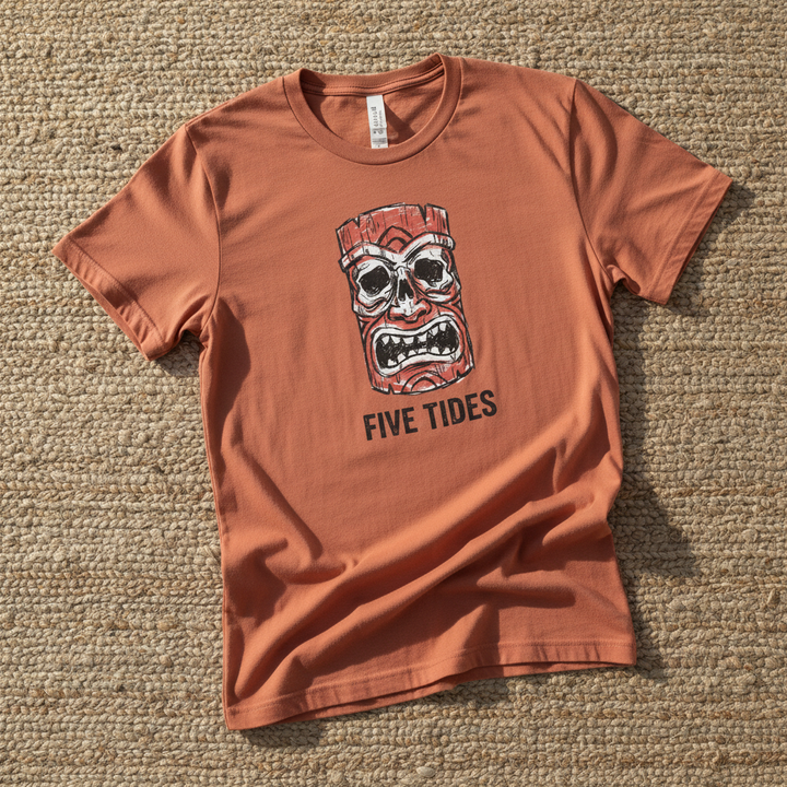Red Tiki Skull FIVE TIDES surf graphic t-shirt in Terracotta casually tossed on a light sand-colored woven rug, coastal lifestyle product photo