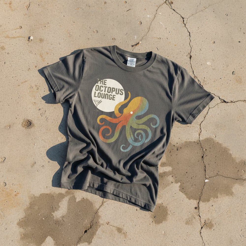 Octopus Lounge graphite garment-dyed tee on light cracked cement with wet marks