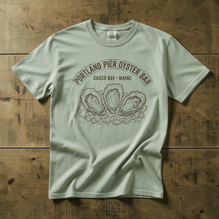 Portland Pier Oyster Bar Casco Bay Maine vintage seafood graphic t-shirt in Bay light green casually tossed on a light sand-colored woven rug, coastal lifestyle product photo
