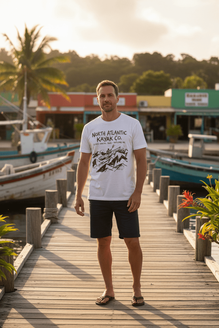 Male model wearing white North Atlantic Kayak Co. t-shirt on tropical island beach town boat dock