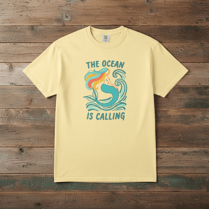 The Ocean Is Calling banana garment-dyed mermaid wave tee laid flat on rustic reclaimed wood