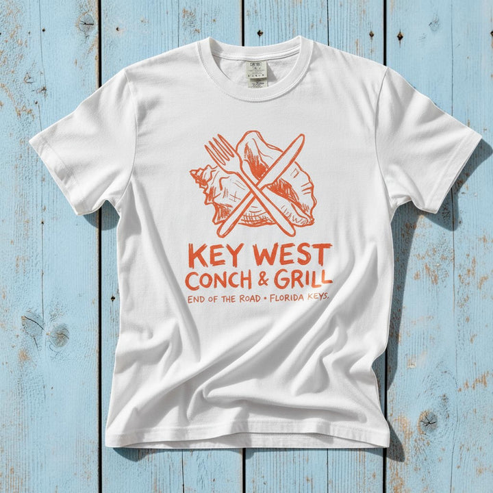 Key West Conch and Grill graphic t-shirt in White with orange graphic casually tossed on a light sand-colored woven rug, Florida Keys lifestyle product photo