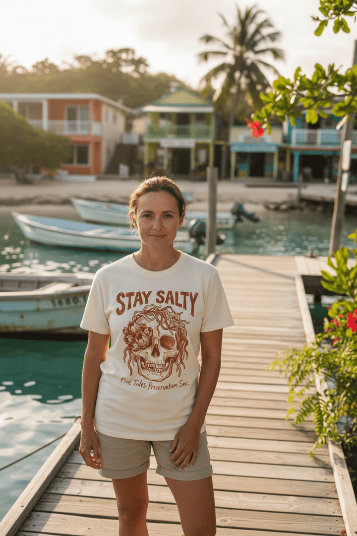 Female model wearing natural ivory Stay Salty Five Tides Preservation Soc. t-shirt on tropical island beach town boat dock