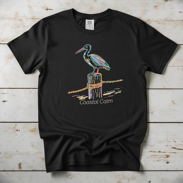 Pelican Pier Coastal Calm black garment-dyed tee on faded driftwood planks