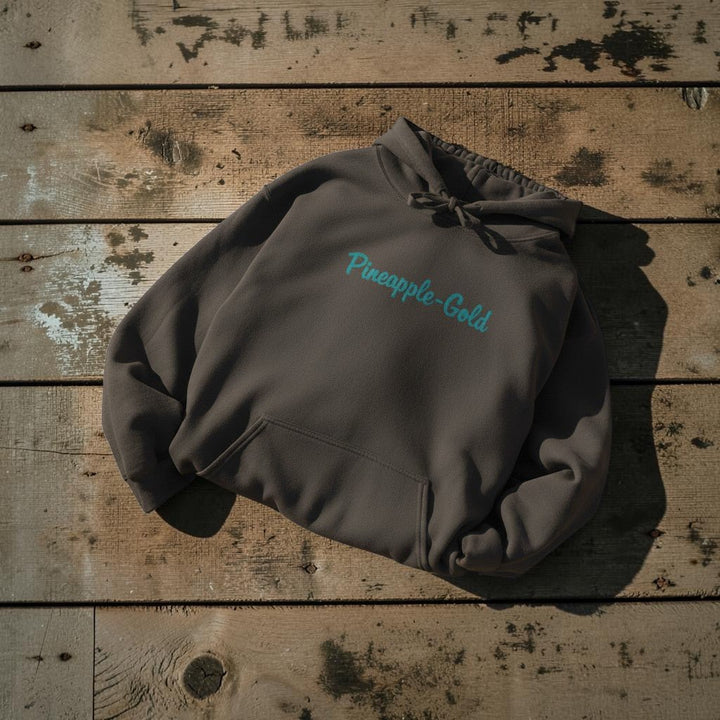 Pineapple-Gold Hoodie in Pepper — front chest graphic, warm sand studio background