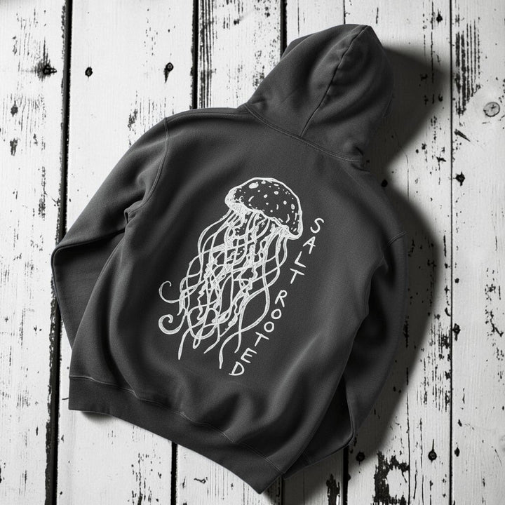Salt Rooted Jellyfish Hoodie in Pepper Charcoal — back graphic with hand-drawn jellyfish and SALT ROOTED lettering on driftwood