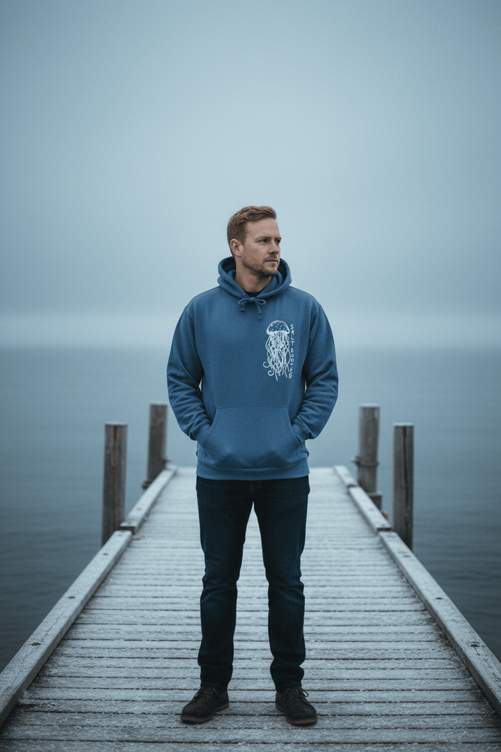 Male model wearing Salt Rooted Jellyfish Hoodie in Blue Jean on a moody Maine winter coastal dock