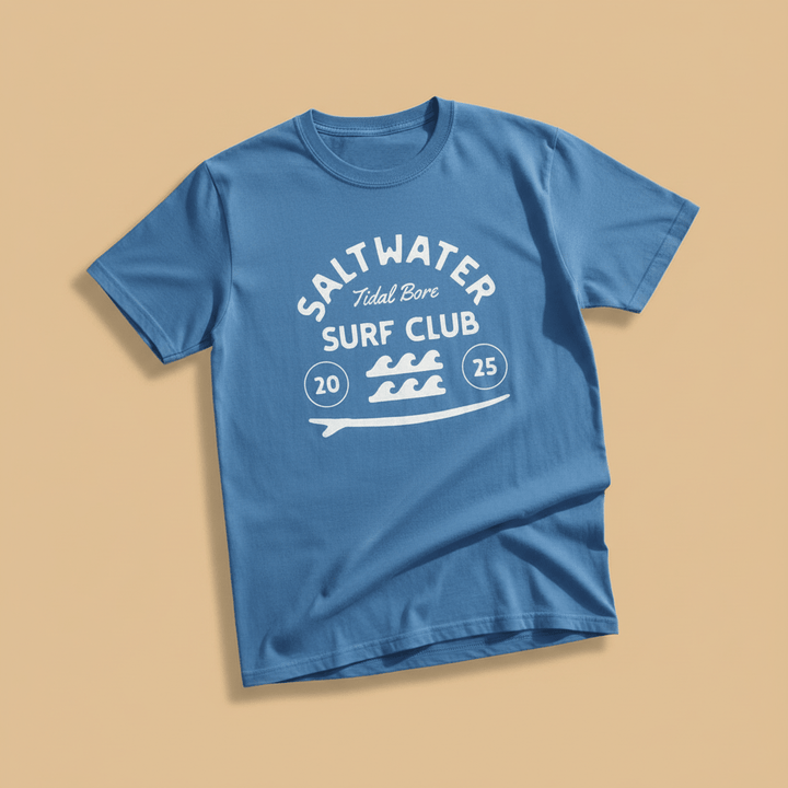 Saltwater Surf Club Tee in Bay Blue — front graphic, warm sand studio background