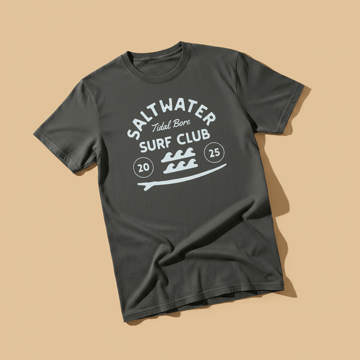 Saltwater Surf Club Tee in Pepper/Charcoal — front graphic, warm sand studio background