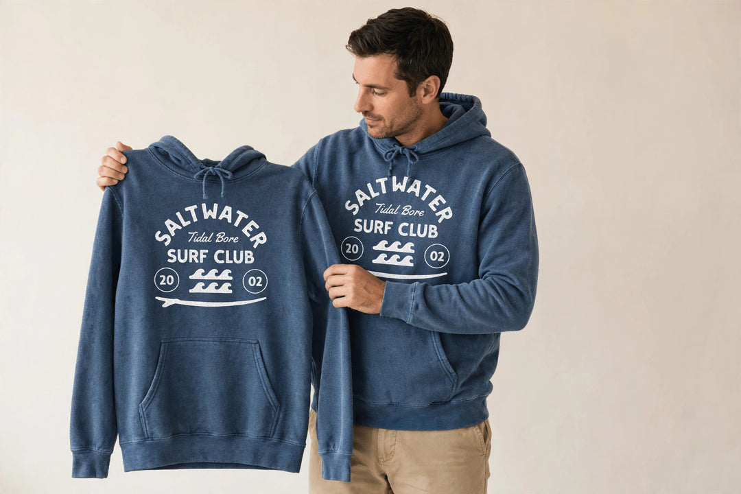 Man wearing the Saltwater Tidal Bore Surf Club Hoodie in Denim, holding up the front print