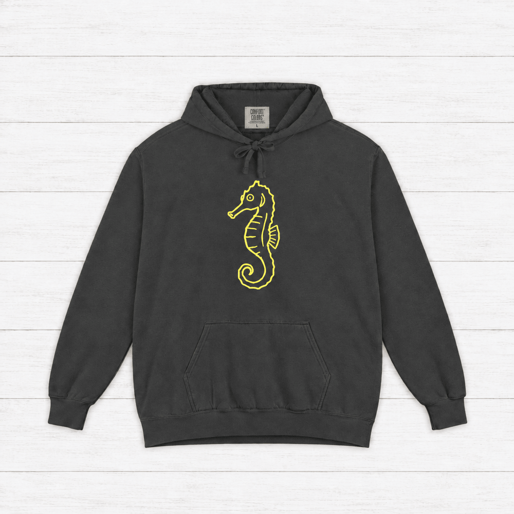 Pepper garment-dyed hoodie front with neon-yellow seahorse chest art, on whitewashed boards.