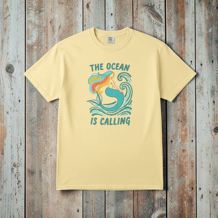 The Ocean Is Calling banana garment-dyed mermaid wave tee laid flat on rustic reclaimed wood