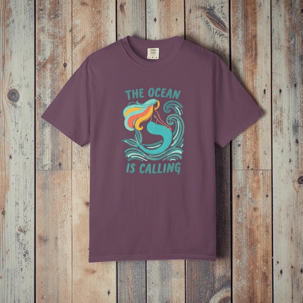 The Ocean Is Calling berry garment-dyed mermaid wave tee laid flat on rustic reclaimed wood