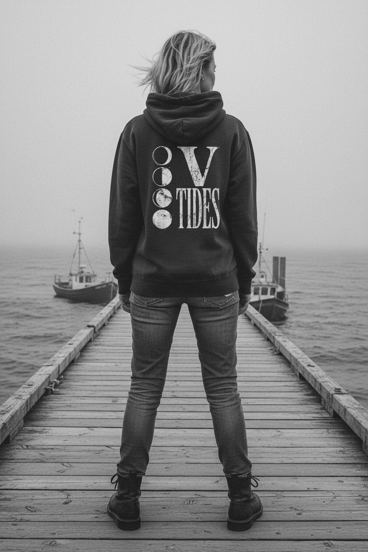 Female model showing back of pepper charcoal V Tides Moon Phases hoodie on grey Maine dock — color pop lifestyle